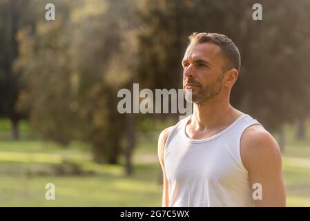 Primo piano di un uomo adulto che indossa un serbatoio bianco che guarda lontano nel parco Foto Stock