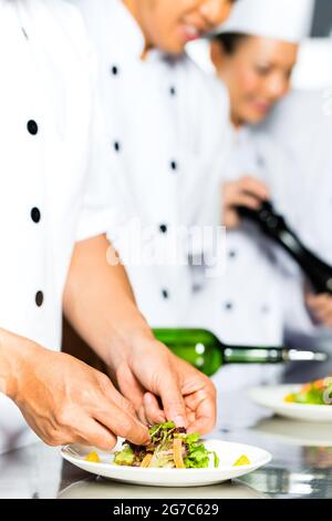 Asian chef indonesiano lungo con altri cuochi nel ristorante o commerciali di hotel cucina cucina, finitura piatto Foto Stock