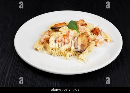 Pesce Pasta con cozze salmone e gamberi con basilico in piatto bianco su sfondo nero di legno. Foto Stock