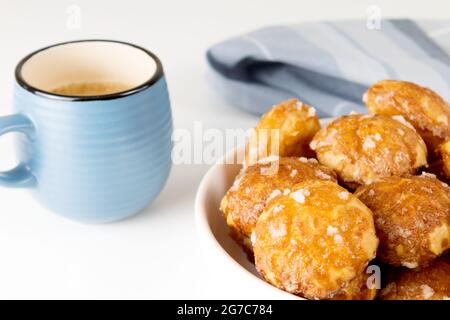 le chouquettes francesi puffs con perle di zucchero sul piatto con la tazza blu di caffè. Pasticceria Choux panetterie francesi classiche. Foto Stock