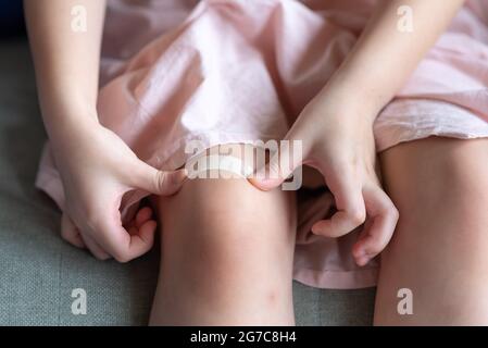 Primo piano di bambini che mettono il bendaggio adesivo di intonaco di corte sul suo ginocchio a casa Foto Stock