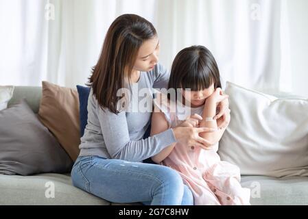 Madre asiatica che mette il bendaggio adesivo dell'intonaco di corte sulla sua figlia a casa Foto Stock