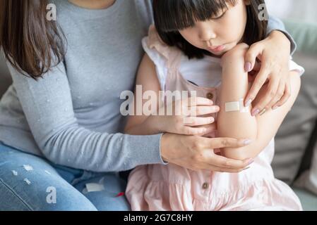 Madre asiatica che mette il bendaggio adesivo dell'intonaco di corte sulla sua figlia a casa Foto Stock