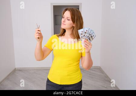 Soldi per un nuovo appartamento con finitura. Una donna con le chiavi della casa e dollari per le riparazioni e l'arredamento del nuovo edificio. Foto Stock