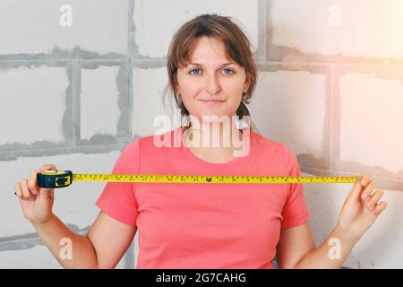 Donna felice con un righello nelle sue mani misura una casa di nuova costruzione. Ricevere un appartamento da una società di costruzione quando si acquista una casa. Foto Stock