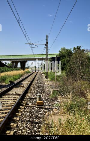 La ferrovia passa sotto un viadotto nella campagna italiana in estate Foto Stock