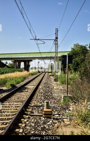 La ferrovia passa sotto un viadotto nella campagna italiana in estate Foto Stock