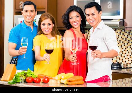 Amici asiatici come tagliare le verdure La cucina insieme in cucina domestica per cena, bere vino Foto Stock