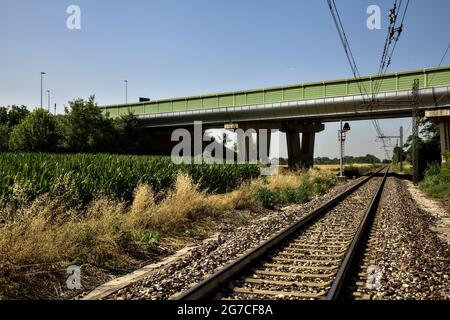 La ferrovia passa sotto un viadotto nella campagna italiana in estate Foto Stock