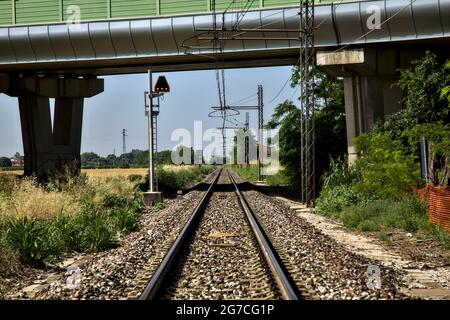 La ferrovia passa sotto un viadotto nella campagna italiana in estate Foto Stock