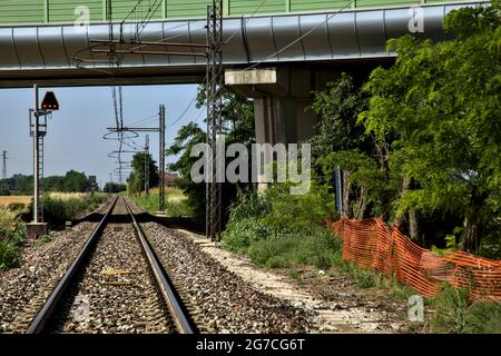 La ferrovia passa sotto un viadotto nella campagna italiana in estate Foto Stock