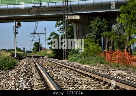 La ferrovia passa sotto un viadotto nella campagna italiana in estate Foto Stock