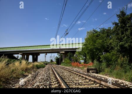 La ferrovia passa sotto un viadotto nella campagna italiana in estate Foto Stock