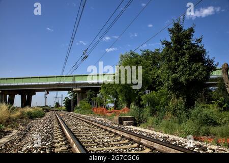 La ferrovia passa sotto un viadotto nella campagna italiana in estate Foto Stock