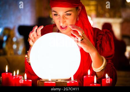 Female fortuneteller o oracolo esoterico, vede in futuro guardando nella loro sfera di cristallo durante una Seance per interpretarli e rispondere alla domanda Foto Stock