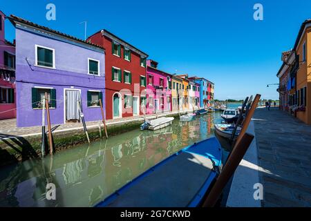 Isola di Burano, laguna di Venezia. Canale con piccole barche e belle case multicolore. Veneto, Italia, Europa. All'orizzonte l'isola di Torcello. Foto Stock