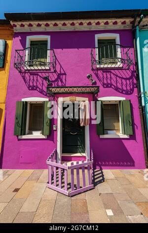 Vecchia piccola bella casa dai colori brillanti (magenta, verde) nell'isola di Burano in una soleggiata giornata di primavera. Venezia, Veneto, Italia, Europa. Foto Stock