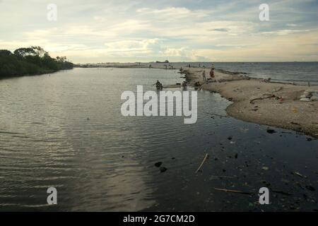 Jakarta, Indonesia. Le persone che hanno tempo libero sulla spiaggia di Cilincing, che si affaccia sulla Baia di Giacarta con traffico del Porto di Giacarta possono essere viste in lontananza. Foto Stock