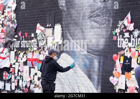 L'artista di strada Akse P19 ripara il murale dell'attaccante del Manchester United e del giocatore d'Inghilterra Marcus Rashford sulla parete del caffè House Cafe su Copson Street, Withington, che è stato vandalizzato dopo che la squadra di calcio inglese ha perso la finale di UEFA Euro 2021. Data immagine: Martedì 13 luglio 2021. Foto Stock