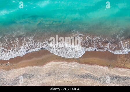 Onde marine che si infrangono su una spiaggia di sabbia gialla, vista dall'alto direttamente sopra Foto Stock