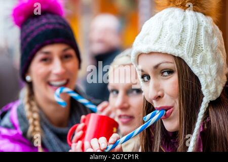 Le donne di bere vino brulé in tazze e mangiando caramelle bastoni tedesco sul mercato di Natale Foto Stock