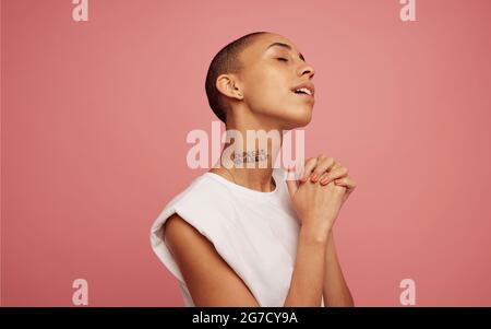 Femmina con testina rasata. Donna androgina con esprimere te scritto sul collo in piedi con i suoi occhi chiusi su sfondo rosa. Foto Stock