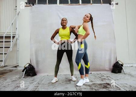 Due donne in outfit fitness guardando la macchina fotografica sul tetto dopo la sessione di allenamento. Le atlete si rilassano dopo aver fatto esercizio sulla terrazza dell'edificio. Foto Stock