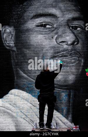 Withington, Manchester, Regno Unito. 13 luglio 2021. L'artista AKSE P19 ripara il suo murale di Marcus Rashford dopo che è stato defaced a seguito della miss di penalità degli attaccanti dell'Inghilterra. La gente aveva previouslt coperto la parte defaced del muro con i messaggi di sostegno. Credit: Howard Harrison/Alamy Live News Foto Stock