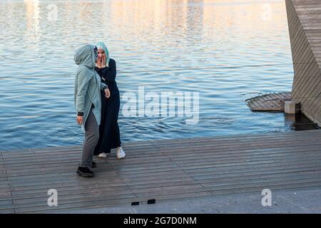 Le donne musulmane si trovano a terra vicino al tranquillo fiume al tramonto Foto Stock