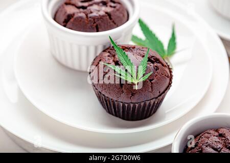Muffin con cupcake di cioccolato alla marijuana e cbd con erbacce. Farmaci per la canapa di marijuana medica nel dessert alimentare. Muffin alle erbe infestate con cannabis e foglie di cannabis serviti Foto Stock