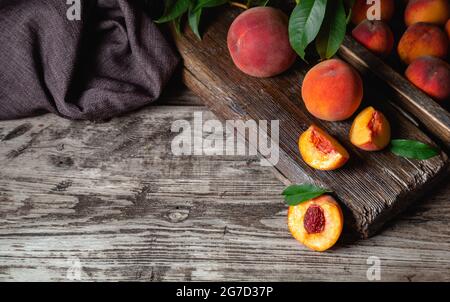 Pesche mature succose su tavolo rustico di legno scuro con spazio copia. Deliziose pesche da fattoria con foglie di frutta intera a metà, pesche con osso. Vita morta Foto Stock