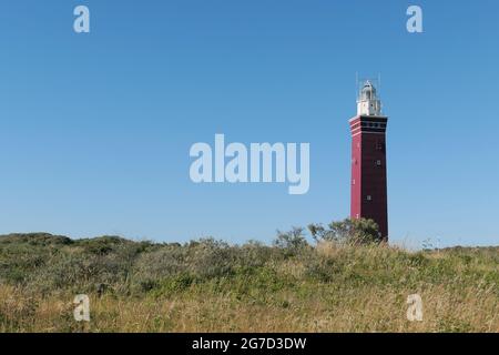 Il faro di Westhoofd (West Head) vicino a Ouddorp, Paesi Bassi, situato in un paesaggio di dune sabbiose, visto contro un cielo blu chiaro. Foto Stock