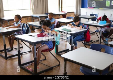 Gruppo di studenti diversi che studiano mentre si siedono sulle loro scrivanie nella classe a scuola Foto Stock