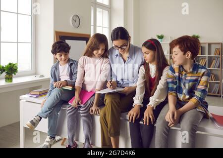 L'insegnante si siede con gli alunni sulla scrivania nelle attività di controllo in classe nel copy-book Foto Stock