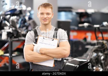 Bel meccanico auto che posa in servizio di auto e che tiene documenti in mani Foto Stock