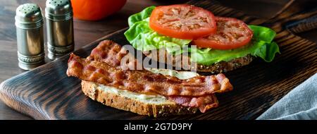 Vista stretta di un panino di pancetta e pomodoro aperto per vedere gli ingredienti, su una tavola di legno. Foto Stock