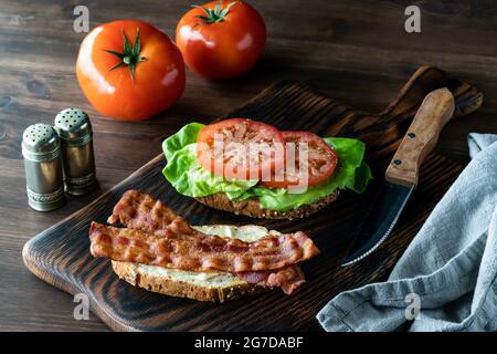 Panino aperto con pancetta e pomodoro su tavola di legno, pronto per mangiare. Foto Stock