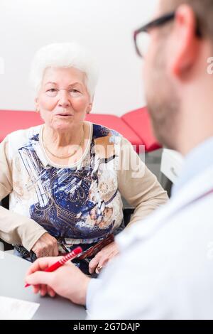 Medico seduto con il titolare di pensione o di rendita in chirurgia consultazione ora a scrivania Foto Stock