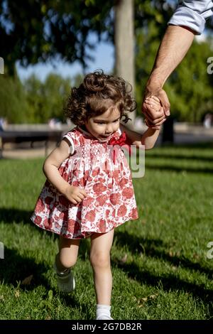 Colpo verticale di una ragazza caucasica carina che cammina tenendo la mano del padre Foto Stock