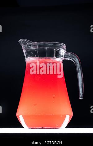 limonata di frutti rossi o bevanda di fragola con ghiaccio in caraffa di vetro su sfondo nero Foto Stock