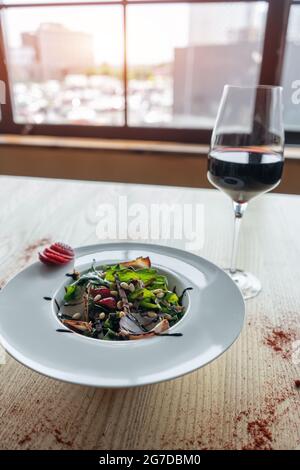 insalata fresca con rucola, prosciutto di carne e fragola e bicchiere di vino rosso a tavola Foto Stock