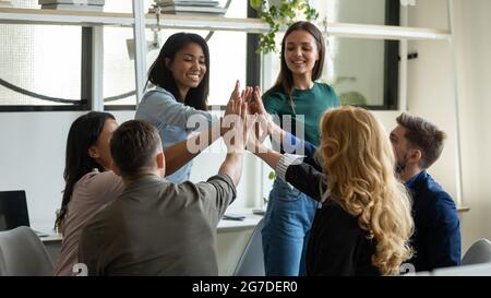 Felice squadra diversificata di successo che dà alto cinque, seduto in cerchio durante la riunione Foto Stock