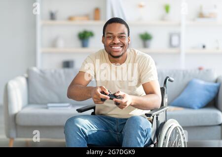 Un simpatico disabile in sedia a rotelle che si diverte a giocare su playstation, divertendosi a casa tua Foto Stock