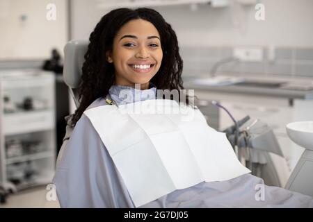 Trattamento stomatologico. Donna afroamericana sorridente seduta nella sedia dei dentisti in clinica Foto Stock