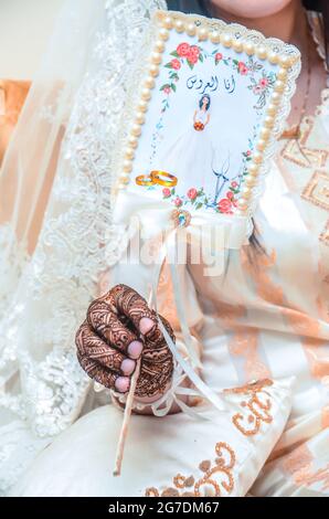 Una sposa marocchina con un tatuaggio di henné sulle sue mani che tiene un segno che dice che sono la sposa Foto Stock