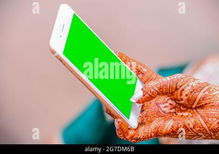 Mano di una sposa tatuata con hennè che tiene un telefono con uno schermo verde Foto Stock