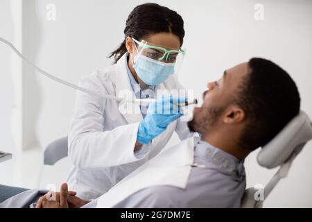 Dentista Signora in maschera medica trattamento dei denti del paziente maschile con Dental Drill Foto Stock