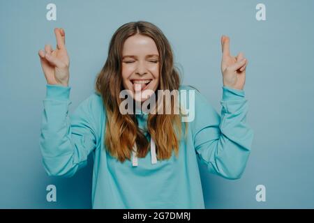 Carino eccitato felice adolescente che tiene le dita incrociate con gli occhi chiusi Foto Stock