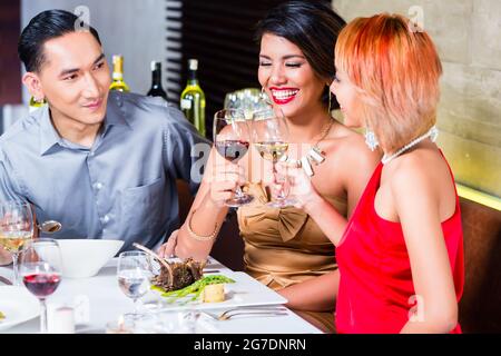 Amici asiatici, due coppie, a pranzo nel ristorante elegante mangiare bene e bere il vino Foto Stock