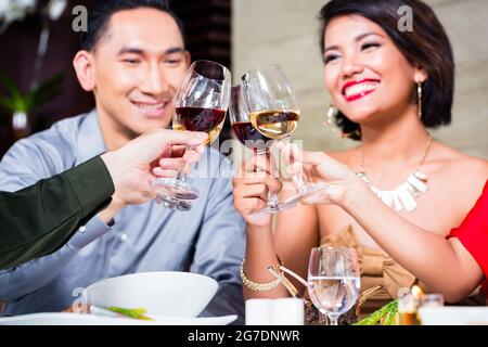 Amici asiatici, due coppie, a pranzo nel ristorante elegante mangiare bene e bere il vino Foto Stock